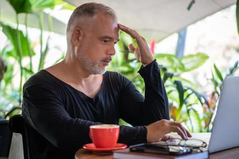 Mature man freelancer working with laptop and phone, red cup of coffee Stock Photos