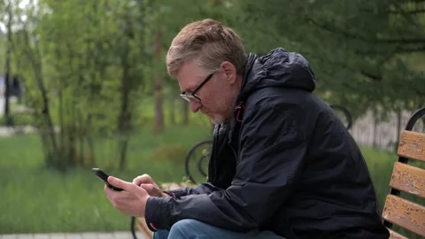 Mature man with glasses using a smartphone on a park bench. closeup. Stock Footage 319812565
