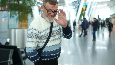 Mature man with a gray beard in a knitted sweater and glasses at the airport or Stock Footage 101178603
