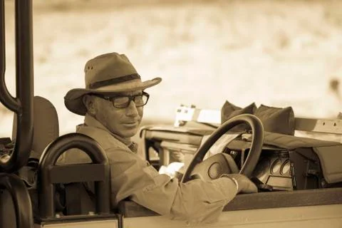 A mature man in hat and glasses in the driving seat of a jeep, sepia tone. Stock Photos