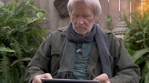 Mature man in his 70s reading a tablet on his lap in his garden Video stock 80498904