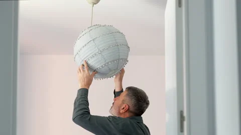 Mature man installing a modern paper lantern in his new apartment Stock Footage 341582065