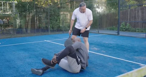 Mature man lunging for ball on backyard court, falling while teammates checking Stock Footage 342031650