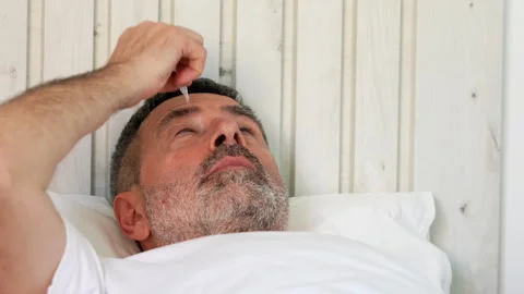 Mature man lying in bed putting eye drops in his eye Stock Footage 341581040