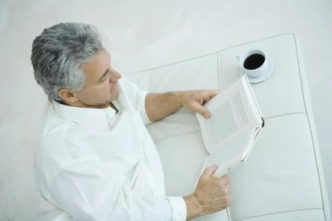 Mature man lying on side next to coffee cup, reading book, high angle view Stock Photos