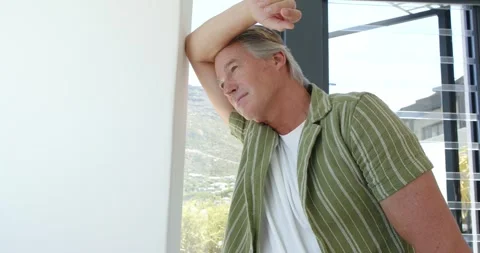 Mature man pausing, leaning on window frame at home, arm over forehead and Stock Footage 336247736
