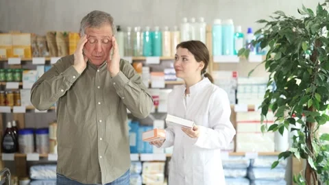 Mature man pharmacy client suffers from headache. Girl pharmacist offer help Stock Footage 329394811