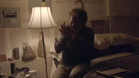 Mature man playing harmonica in a dimly lit bedroom Stock Footage 331659549