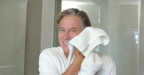 Mature man post-shower, holding white towel, dabbing face, drying hair at vanity Stock Footage 335131545