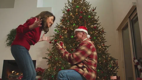 A mature man proposes on one knee near a decorated tree and fireplace. Stock Footage 340927751