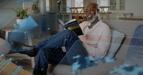 Mature man reading book on sofa, tech map overlay drifting causing page turn and Stock Footage 322203126