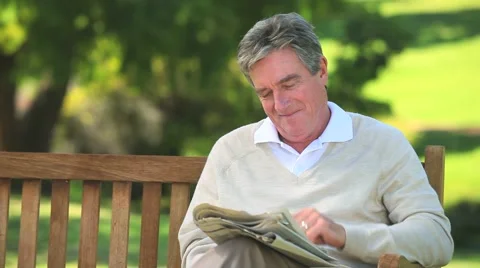 Mature man reading a newspaper on a bench Stock Footage