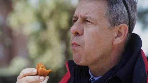 Mature man in a red jacket with a big appetite eat the suppli ' in the street Stock Footage 100937895