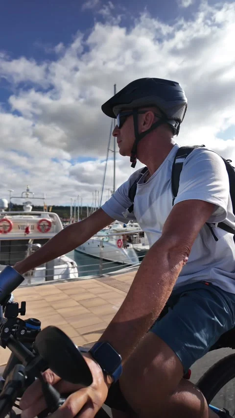 Mature man riding an e-bike along a sunny marina Stock Footage 344816273