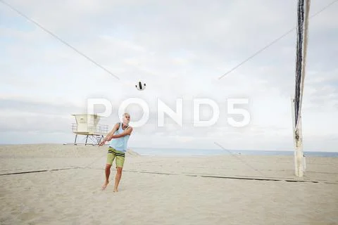 Mature Man Standing On A Beach, Playing Beach Volleyball.
