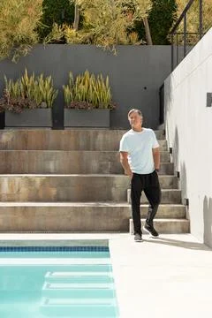 Mature man standing on pool deck near terraced steps wearing pale tee checking Stock Photos