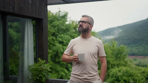 Mature man standing in tiny house terrace in front of beautiful nature with cup Stock Footage 205870057