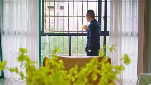 Mature man stands in front of a security window drinking tea. Stock Footage 320093109