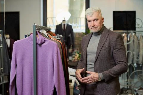 A mature man in a suit is posing while choosing a sweater in a clothing store Stock Photos