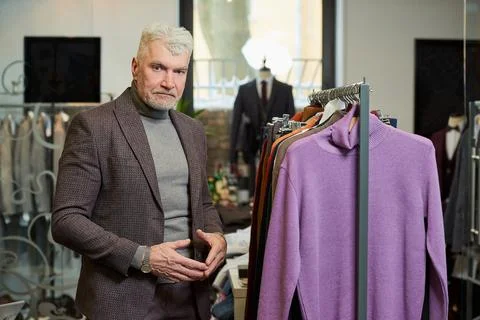 A mature man in a suit is posing while choosing a sweater in a clothing store Stock Photos