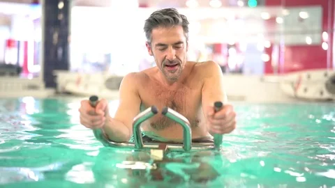 Mature man in swimming-pool doing aquabike exercises Stock Footage 72708656