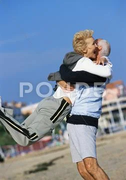 Mature Man Swinging Mature Woman On Beach