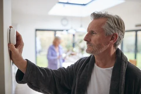 Mature Man Turning Control Dial On Digital Central Heating Thermostat At Home Stock Photos