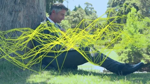 Mature man typing on laptop under tree, activating yellow wireframe and Stock Footage 333671071