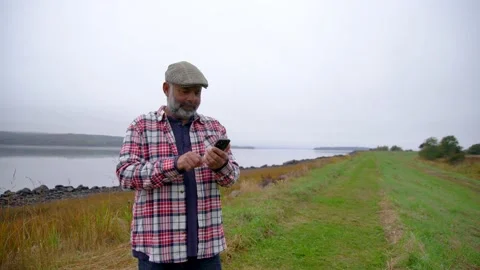 A mature man using a cell phone during a walk with his dog on the coast Stock Footage 162968692