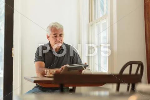Mature Man Using Digital Tablet In Country Store Cafe