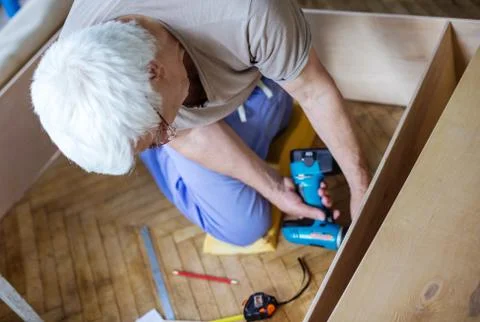 Mature man using electric screwdriver while making bookcase or shelf unit Stock Photos