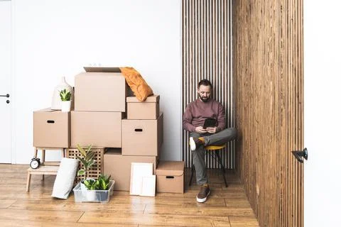 Mature man using his tablet, unpacking things from boxes while moving in new Stock Photos
