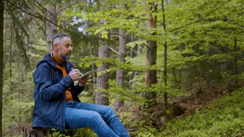 Mature man using laptop in forest in nature, outdoor office concept. Stock Footage 131582100