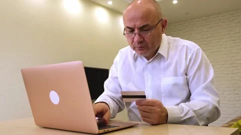 Mature man using laptop holding credit card making secure online payment Stock Footage 322725668
