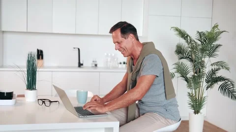 Mature man using laptop, making video call, sitting at table in kitchen, senior Stock Footage 219620174