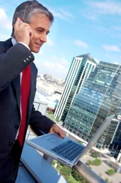 Mature man using mobile phone and laptop in balcony Stock Photos