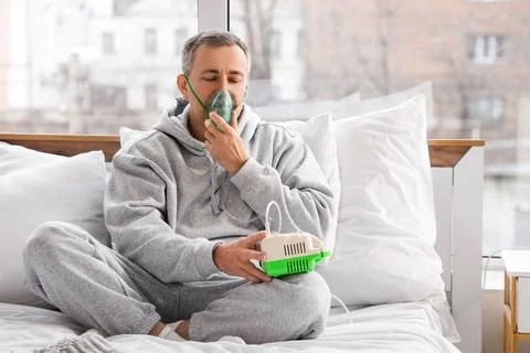 Mature man using nebulizer in bedroom Stock Photos