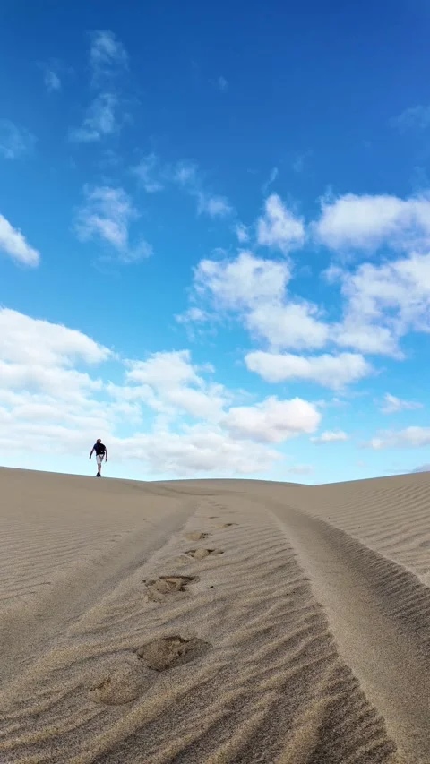Mature man walking alone on sand dunes under a blue sky Stock Footage 346177624