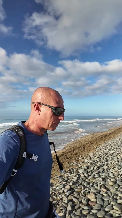 Mature man walking along a pebble beach in slow motion Stock Footage 346177524