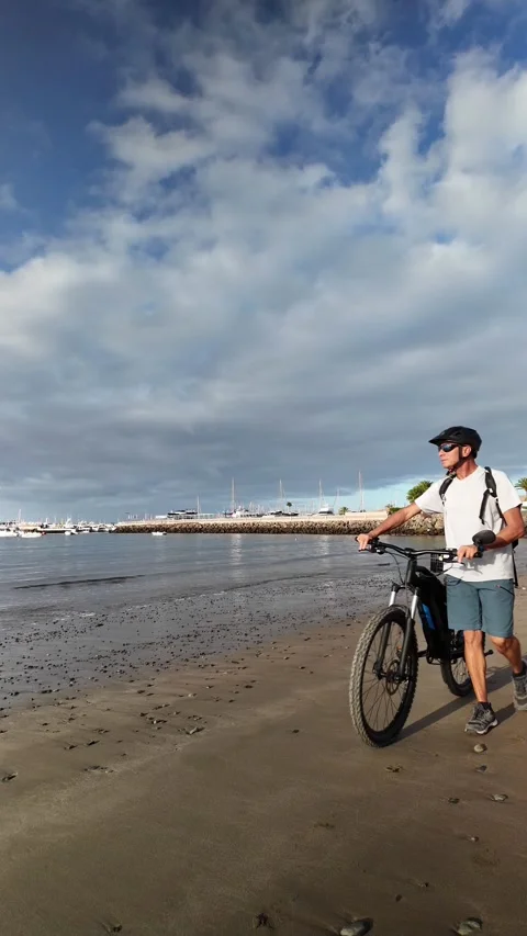 Mature man walking with his electric bicycle on the beach sand Stock Footage 344816264