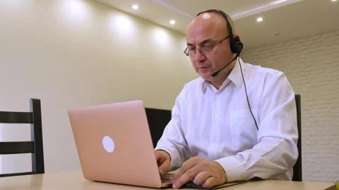 Mature man wearing headset talking working remotely on laptop Video stock 322778824