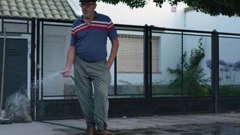 Mature man whistles with joy while watering sidewalk of his home. South Ame.. Stock Footage 283495481