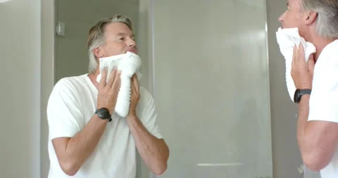 Mature man in white tee raising folded towel, pressing and drying face at Stock Footage 342801792