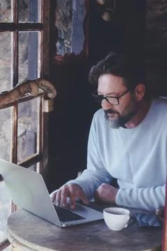 Mature man at work on laptop computer sitting at the table inside a home co.. Foto stock