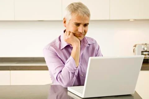 Mature man working on a laptop in the kitchen Stock Photos