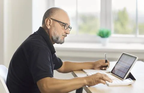Mature man working with spreadsheet on tablet and calculator at home office Stock Photos
