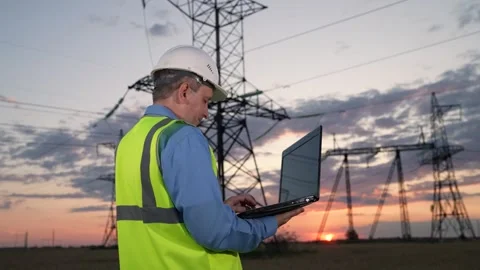 Mature manager sets up power transmission lines equipment via laptop in evening Stock Footage 260189873