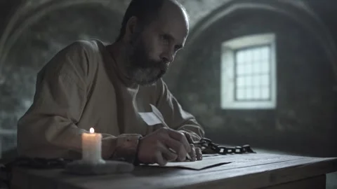 Mature medieval man in chains pausing his writing, staring ahead thoughtfully 스톡 동영상 339231731