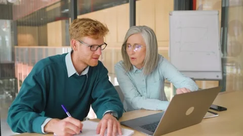 Mature mentor teaching intern, explaining online job using laptop in office. Stock Footage 201860624