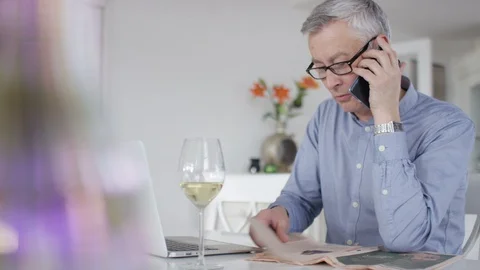 Mature older man on laptop takes a call on his cell phone Stock Footage